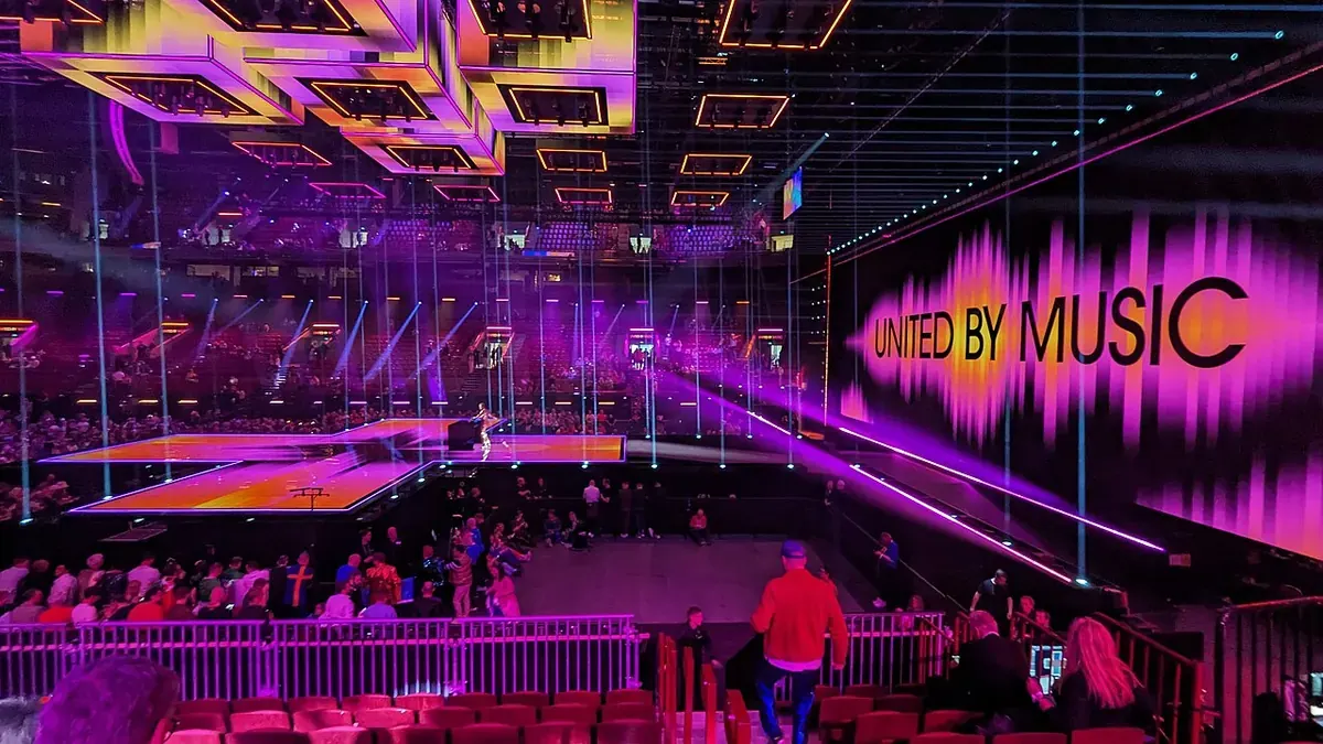 Сцената на Евровизия 2024 с лилаво осветление, светещ надпис „United by Music“ и публика в залата