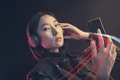 Жена със слушалки и кожено яке държи смартфон, около телефона има червени светлинни линии, тъмен фон